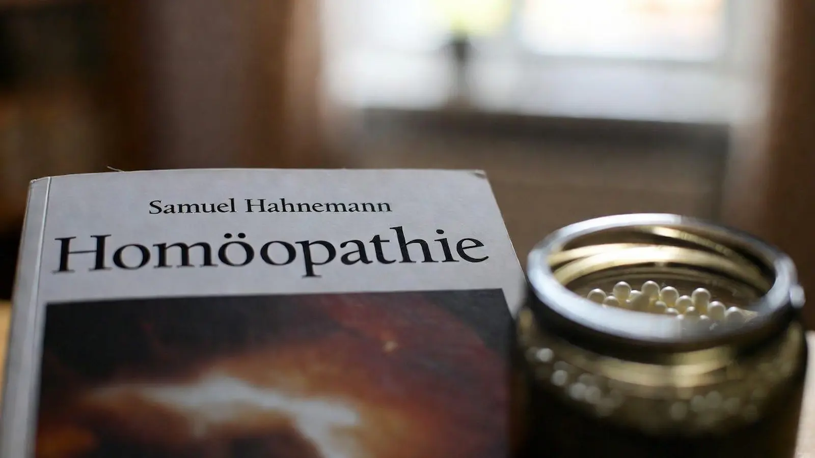 Buch zur Homöopathie von Samuel Hahnemann neben einem Glas mit Globuli
